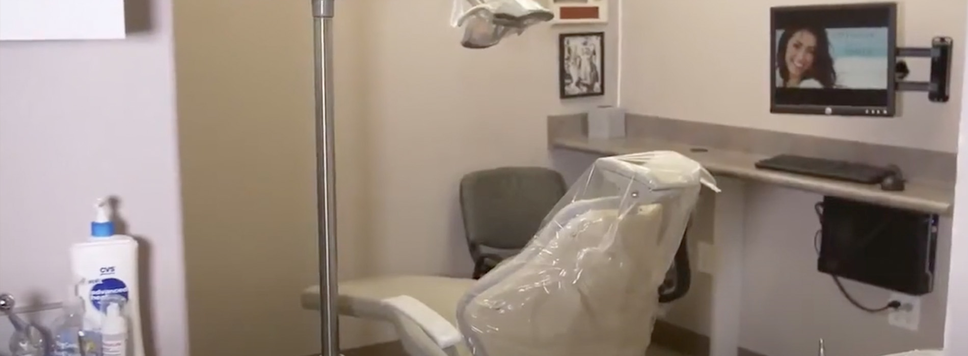The image shows a dental chair in a small room with a monitor and a desk, suggesting a dental office setting.