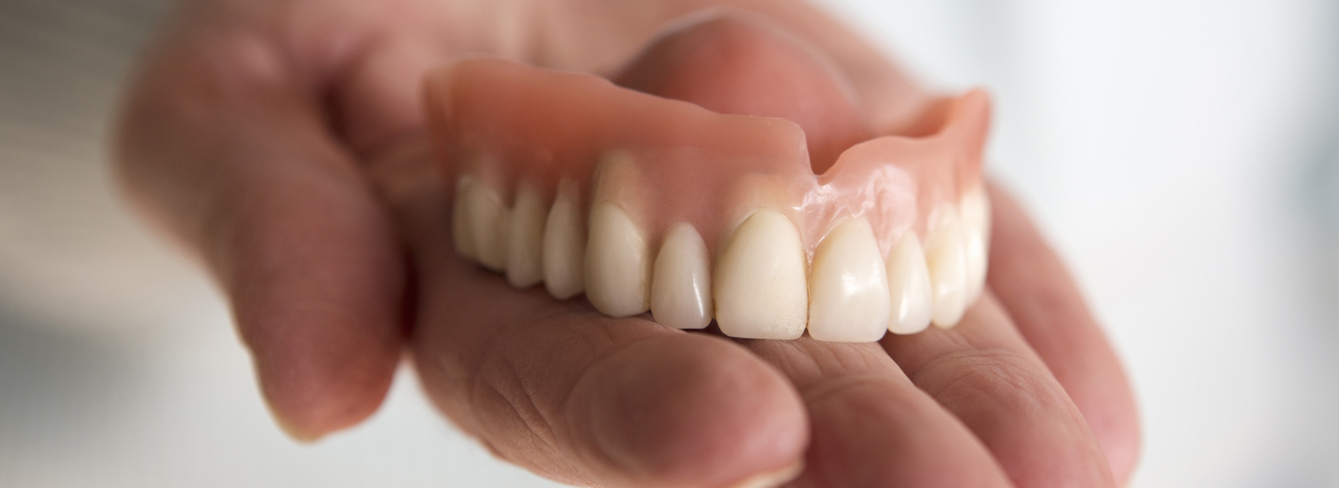 An individual s hand holding a set of dentures with visible teeth.