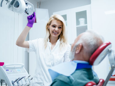 A dental professional, likely a dentist or hygienist, is assisting an elderly patient with a medical device in a dental office.