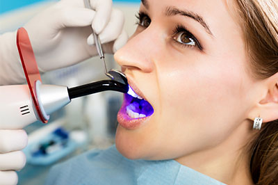 The image shows a person sitting in a dentist s chair with an electronic device attached to their mouth, likely for dental treatment or examination.