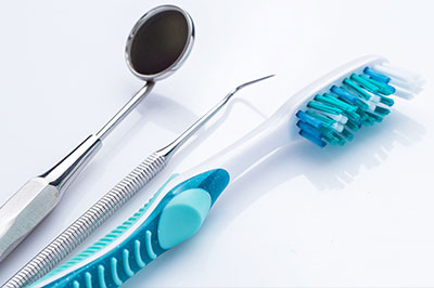 The image displays a collection of dental tools, including a toothbrush with blue bristles, a pair of tweezers, and a small dental mirror, all arranged on a white surface.