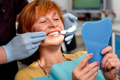 The image shows a woman sitting in a dental chair, receiving dental care with a smile on her face.