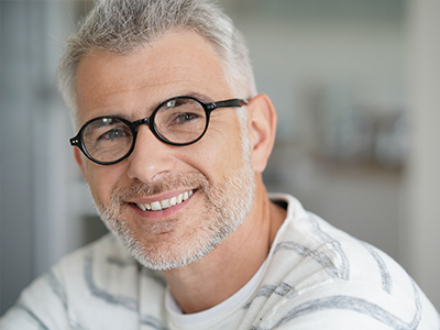 The image shows a man with glasses, smiling at the camera.