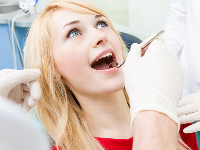 A woman in a dental chair receiving dental care, with a dentist performing the procedure and assistants observing.